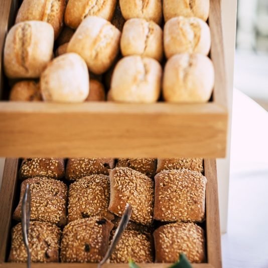 Bread buns in abundance on display at slatted shelf fixture in hotel or supermarket for sale