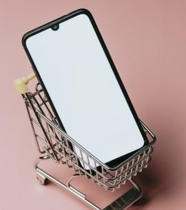 Shopping cart with a blank mobile phone over a pastel pink background, e commerce
